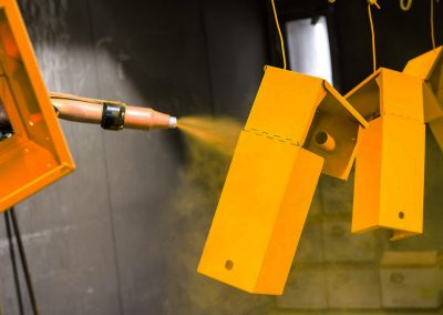 An image of a spray gun spraying orange powder coating onto metal parts.